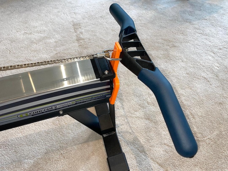 May include: A Concept2 Model D rowing machine, with a navy blue handle and orange details. The machine has a silver rail and a black frame. The text "Concept 2 Model D" is visible on the side.