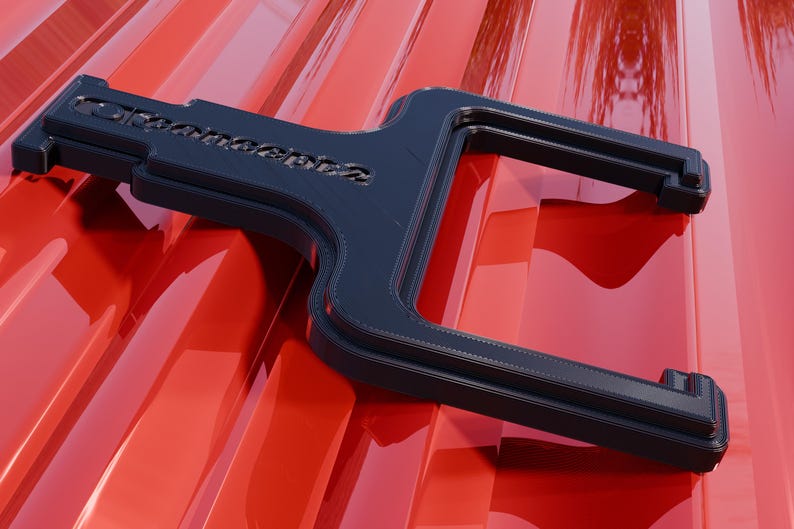 May include: A dark blue, Y-shaped object with the word "Dromconcepts" etched into its surface, resting on a glossy red surface. The object has a layered design and appears to be made of plastic or a similar material.