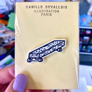 Peut inclure: Une illustration en noir et blanc d'un petit chariot en bois avec des roues. L'illustration est imprimée sur une carte jaune avec le texte "Camille Devallois Illustration Paris".