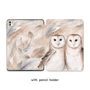 Könnte beinhalten: Eine Tablethülle mit einer Aquarellillustration von zwei Schleiereulen, die nebeneinander vor einem Hintergrund aus weichen beigen und grauen Federn sitzen. Das Etui verfügt über einen Kameraausschnitt und einen Stifthalter für einen Eingabestift.