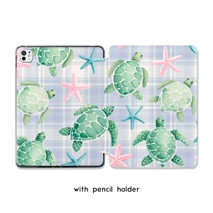 May include: A tablet case with a watercolor design featuring green sea turtles and pink and blue starfish on a light blue plaid background. The case has a pencil holder and is open, displaying the tablet screen.