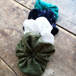 May include: Four scrunchies in different colors, green, black, white, and olive green, with gold glitter dots. The scrunchies are made of a soft, stretchy fabric.