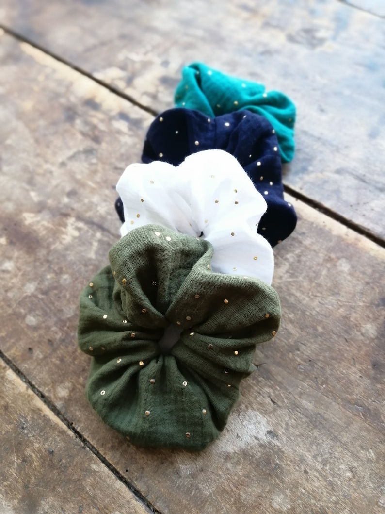 May include: Four scrunchies in different colors, green, black, white, and olive green, with gold glitter dots. The scrunchies are made of a soft, stretchy fabric.