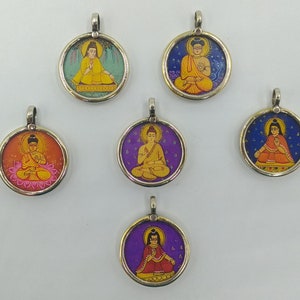 May include: A collection of six round pendants with silver-colored metal frames. Each pendant features a colorful illustration of a seated figure, likely a Buddha, against a background of various colors, including yellow, orange, purple, and blue. The pendants have a small loop at the top for a chain.