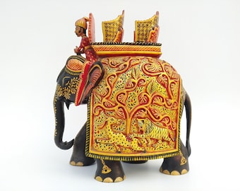 Könnte beinhalten: Handgeschnitzte Holz-Elefantenfigur, schwarz, rot und gold bemalt. Der Elefant hat aufwendige Schnitzereien und einen Reiter in traditioneller Kleidung. Die Decke des Elefanten zeigt eine detaillierte Dschungelszene mit Tieren.