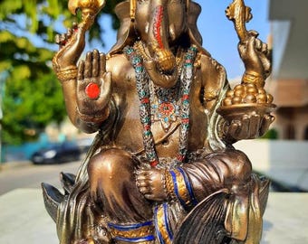 Könnte beinhalten: Bronzefarbene Statue der hinduistischen Gottheit Ganesha, sitzend auf einer Lotusblume. Die Statue weist aufwendige Details auf, darunter eine Krone, Schmuck und mehrere Arme, die verschiedene Gegenstände halten. Die elefantenköpfige Figur hat einen roten Punkt auf der Handfläche.