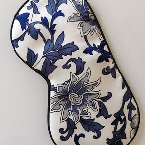 May include: A white sleep mask with a blue floral pattern. The mask has a black elastic band.
