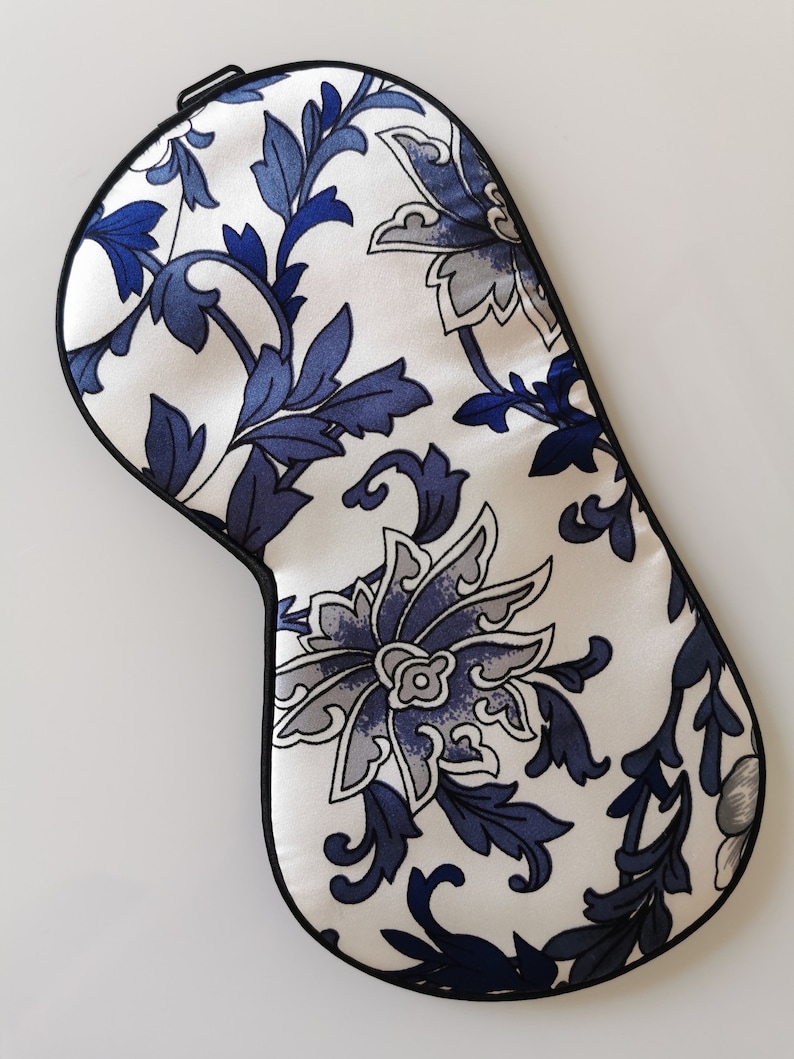 May include: A white sleep mask with a blue floral pattern. The mask has a black elastic band.