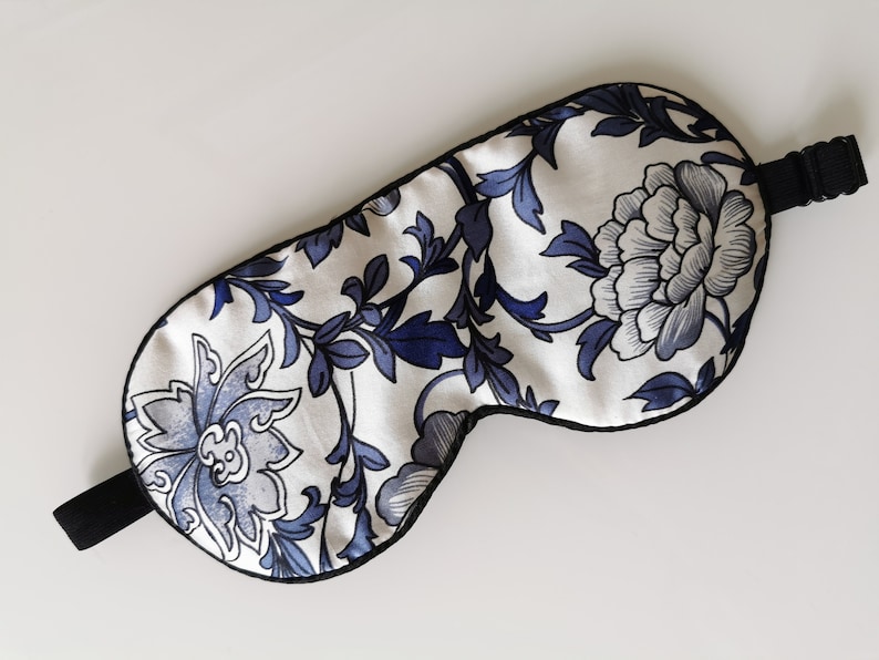 May include: A white sleep mask with a blue and white floral pattern. The mask has an adjustable strap.
