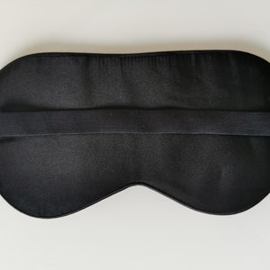 May include: Black sleep mask with an adjustable elastic strap. The mask is made of a soft, smooth fabric.
