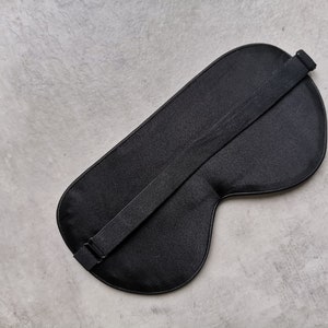 May include: A black sleep mask with an adjustable strap. The mask is made of a soft, smooth fabric.