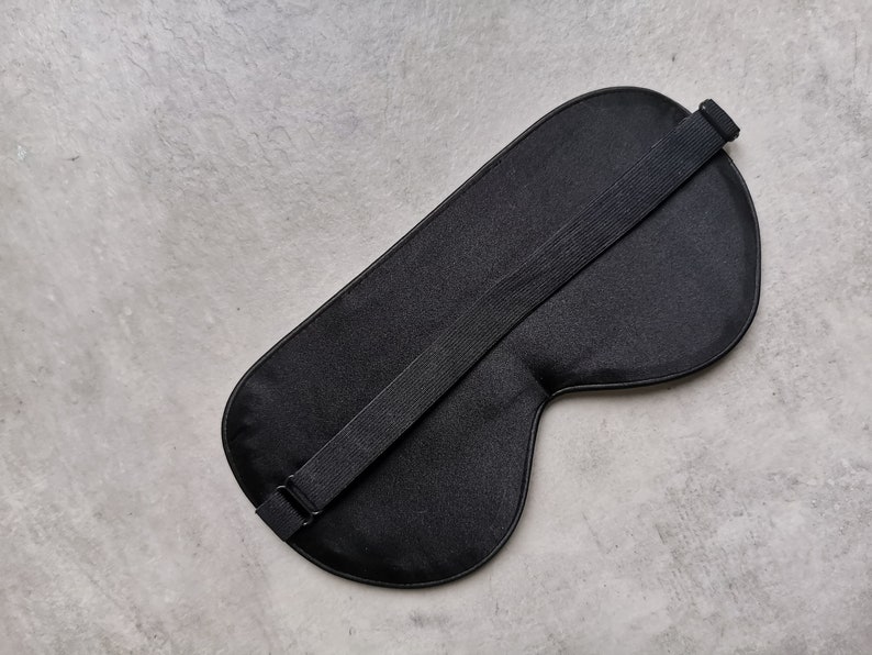 May include: A black sleep mask with an adjustable strap. The mask is made of a soft, smooth fabric.