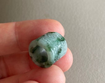 Puede incluir: Una cuenta de jade verde con un agujero en el centro. La cuenta es lisa y pulida.