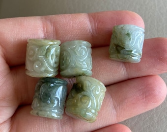 May include: Five green jade beads with intricate carved designs. The beads are cylindrical in shape and have a smooth, polished finish.