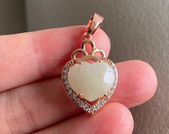 Puede incluir: Un colgante en forma de corazón de oro rosa con una piedra blanca y detalles de cristal transparente.