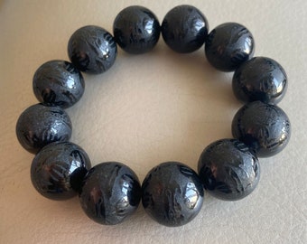 May include: A black beaded bracelet with a glossy finish. Each bead has a carved design.