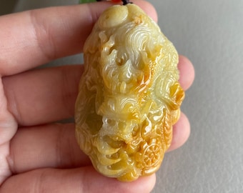 May include: A yellow jade pendant carved with a detailed dragon design. The pendant is attached to a brown cord with green and red beads.