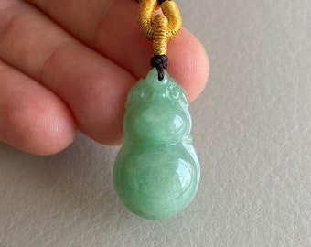 May include: A green jade gourd pendant on a black cord with gold accents. The pendant is carved in the shape of a gourd, a symbol of good fortune and prosperity in Chinese culture.