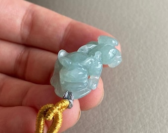 May include: A jade green pendant carved in the shape of a mythical creature, hanging from a braided cord with gold accents.