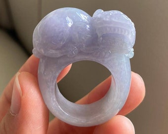 May include: A lavender jade ring carved with two intertwined dragons. The ring is made of a smooth, polished jade and has a delicate design.
