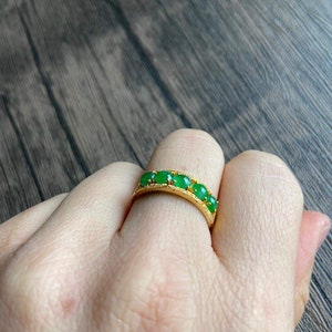 May include: A gold band ring with five green jade stones set in the band.