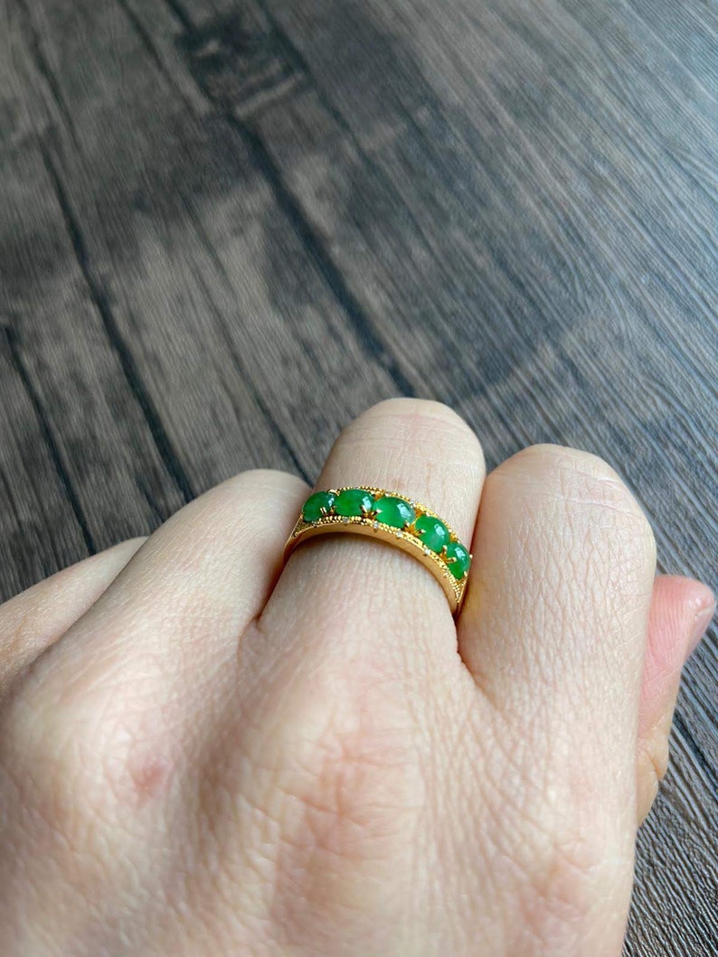May include: A gold band ring with five green jade stones set in the band.