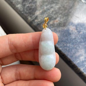 May include: A jade pendant with a three-section design, featuring a gradient of white and light green hues. The pendant is suspended from a gold-coloured bail.