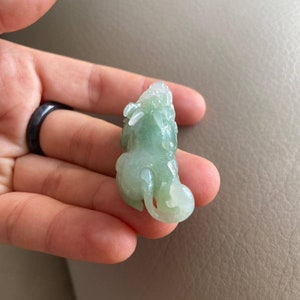 May include: A green jade pendant carved in the shape of a mythical creature. The pendant is detailed and intricate, with a smooth, polished finish.
