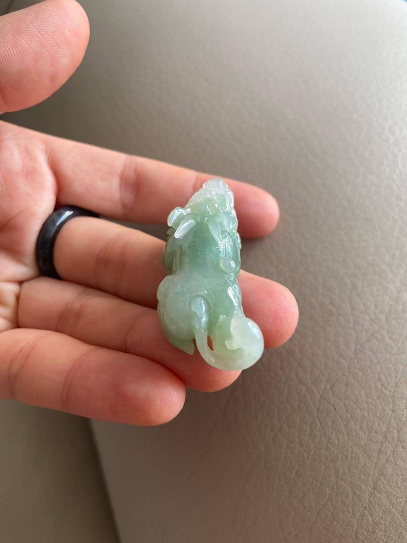 May include: A green jade pendant carved in the shape of a mythical creature. The pendant is detailed and intricate, with a smooth, polished finish.