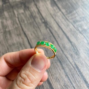 May include: A gold band ring with five green oval-shaped gemstones set in the band.