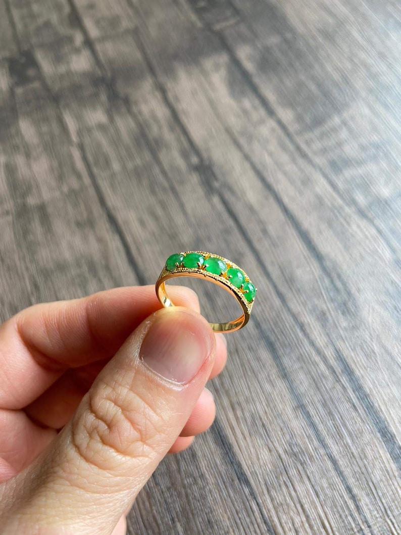 May include: A gold band ring with five green oval-shaped gemstones set in the band.