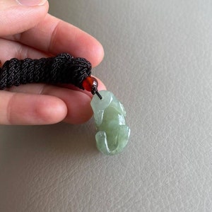 May include: A jade green frog pendant carved from jade with a black cord and a red bead.