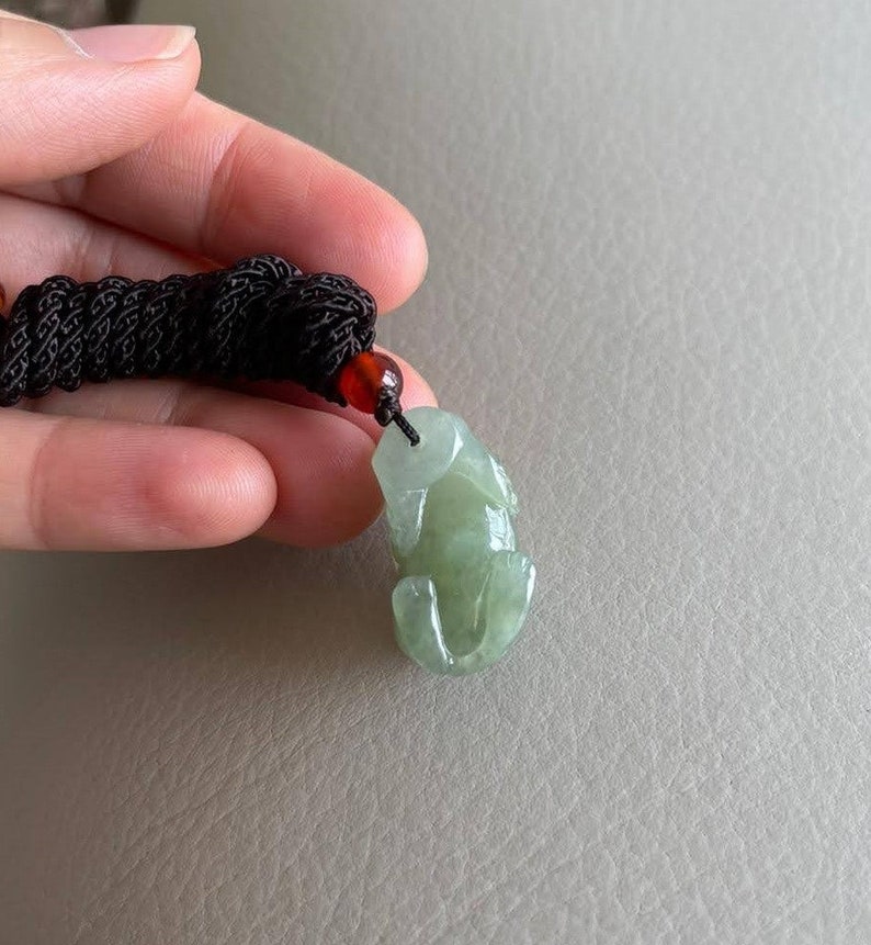 May include: A jade green frog pendant carved from jade with a black cord and a red bead.