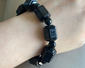 May include: Black bracelet with square beads featuring Chinese characters. Each bead is separated by a smaller black bead.