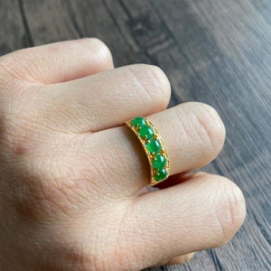 May include: A gold ring with a row of oval-shaped green gemstones set in a gold band. The ring is on a person's finger.
