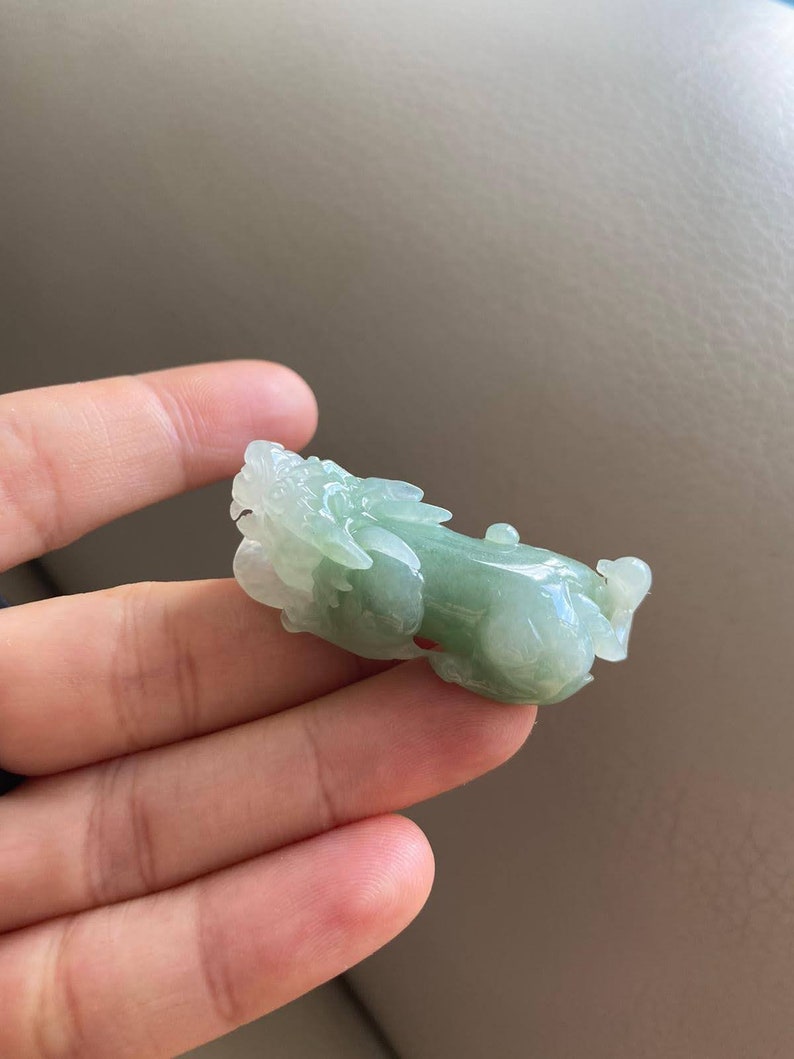 May include: A green jade carving of a mythical creature, possibly a dragon or a lion, with intricate details. The carving is smooth and polished, and the jade has a translucent quality.
