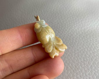 Puede incluir: Un colgante de jade amarillo tallado en forma de pez. El colgante está unido a una cadena de oro.