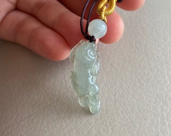 May include: A jade green pendant carved in the shape of a dragon, hanging from a brown cord with a gold and brown knot and a jade green bead.