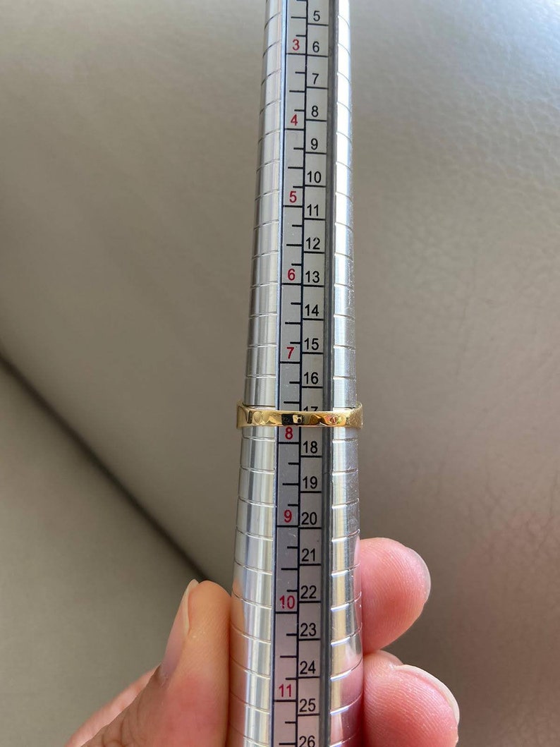 May include: A gold ring being measured on a metal ring sizer. The ring sizer has markings from 5 to 26.
