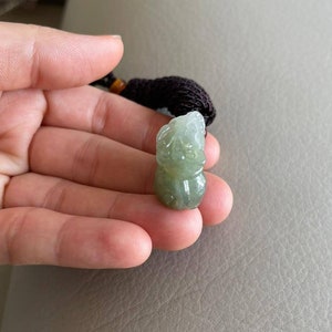 May include: A green jade pendant carved in the shape of a mythical creature. The pendant is attached to a brown cord.