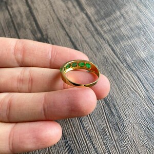 May include: A gold band ring with a row of emerald green gemstones.