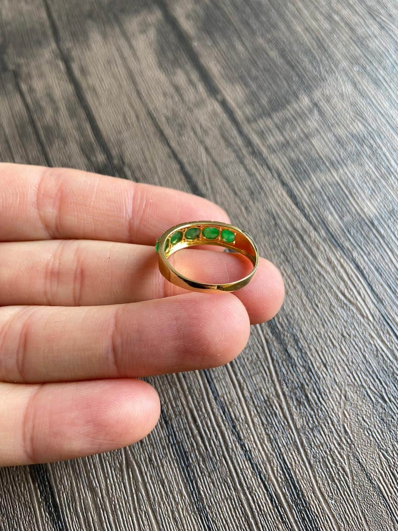 May include: A gold band ring with a row of emerald green gemstones.