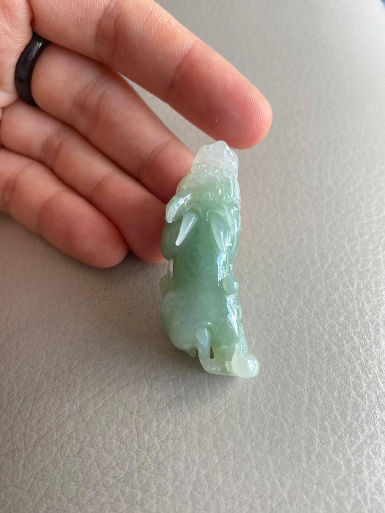 May include: A green jade pendant carved in the shape of a dragon. The pendant is translucent and has a light green color.