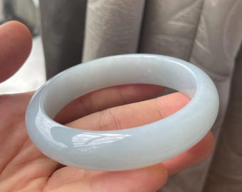 Pode incluir: Uma pulseira de jade verde pálido. A superfície lisa e polida reflete a luz, mostrando as variações naturais de cor. O design circular é um estilo clássico de joalharia.