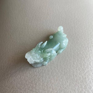 May include: A jade green dragon pendant carved from jade. The dragon is in a curled position with its head raised and its tail curled around its body.
