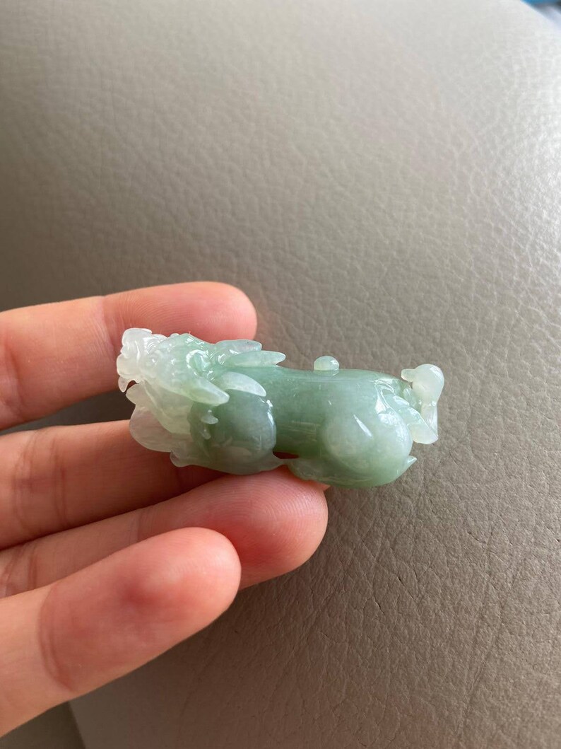 May include: A jade green carved jade pendant in the shape of a mythical creature. The pendant is detailed and has a smooth, polished finish.