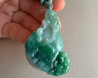 May include: A green jade pendant carved in the shape of a mythical creature with intricate details. The pendant is suspended from a light green cord.