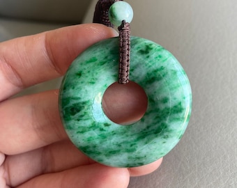 May include: A green jade pendant in the shape of a donut, with a brown cord attached.