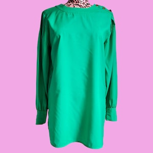 May include: A long-sleeved, green blouse with a round neckline and button accents on the shoulders.