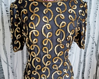 May include: A black sequined dress with gold embellishments in a swirling pattern. The dress has short sleeves and a round neckline.